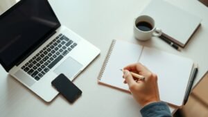 Bureau sobre avec ordinateur portable et main tenant un stylo, illustrant le choix d’un courtier en Bourse